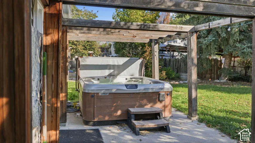 Outdoor hot tub situated on a concrete patio under a wooden pergola, featuring an attached step unit and expansive backyard lawn