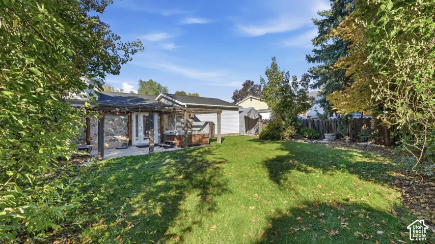 Backyard featuring a paved patio, wooden pergola, mature trees, lawn, and perimeter wood fencing