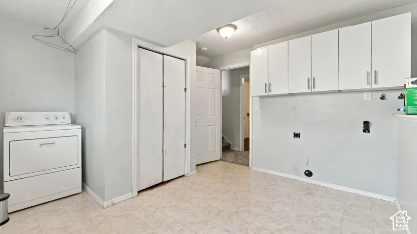 Laundry area featuring tile flooring, white shaker-style wall-mounted cabinetry, and dual-panel closet doors
