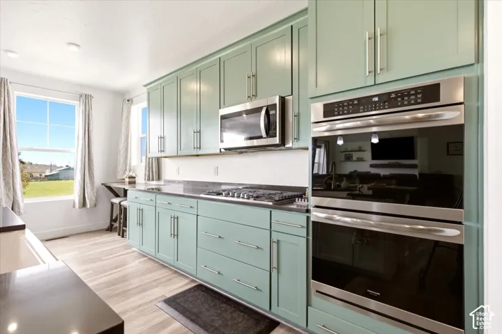 Kitchen featuring pale green shaker-style cabinetry, stainless steel double wall ovens, gas cooktop, built-in microwave, and wood-finish flooring