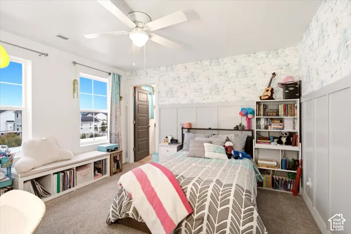Bedroom featuring patterned wall covering, half-height wainscoting, built-in window seat with integrated storage, and a central ceiling fan with integrated light fixture