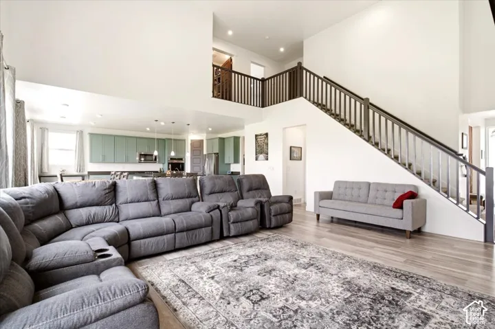 Open-concept floor plan featuring soaring double-height ceilings, a staircase with a stained-wood railing, recessed lighting, and wood-finish flooring