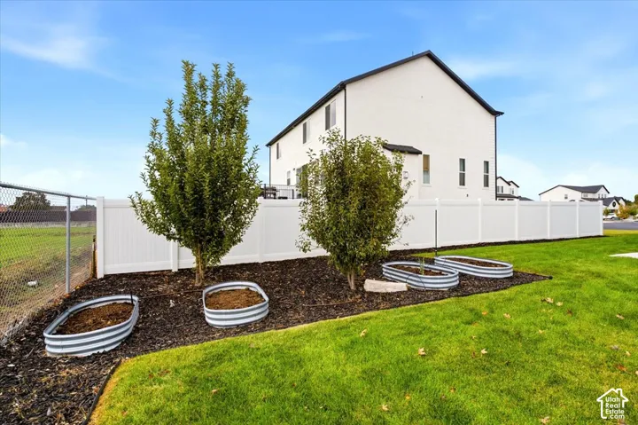 Backyard featuring corrugated metal garden beds, mulched landscaping, mature trees, and white vinyl privacy fencing