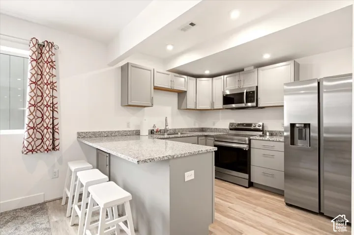 Kitchen featuring light grey shaker-style cabinetry, stone-surface countertops, stainless steel appliances, and wood-finish flooring