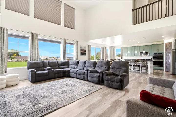 Open-concept interior featuring double-height ceilings, expansive windows, wood-finish flooring, a kitchen island with bar seating, and a second-level overlook with decorative railing
