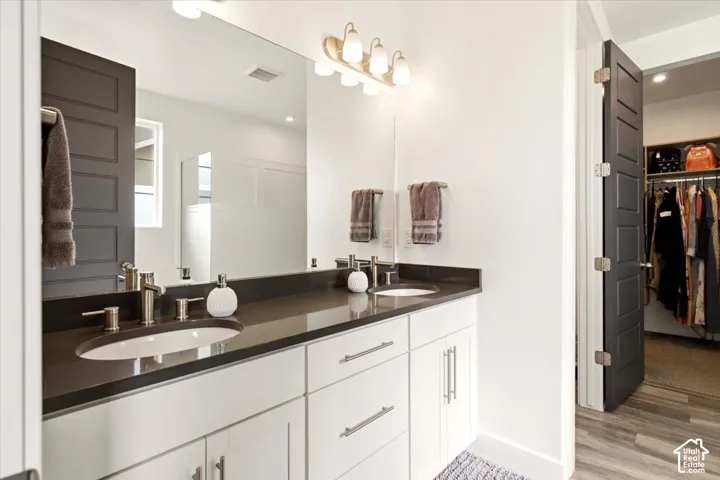 Bathroom featuring a dual-sink vanity with dark stone countertops, shaker-style cabinetry, wall-mounted light fixtures, and a large plate-glass mirror