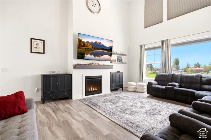 Living area featuring high ceilings, a gas fireplace with a mantel, large windows, and wood-finish flooring