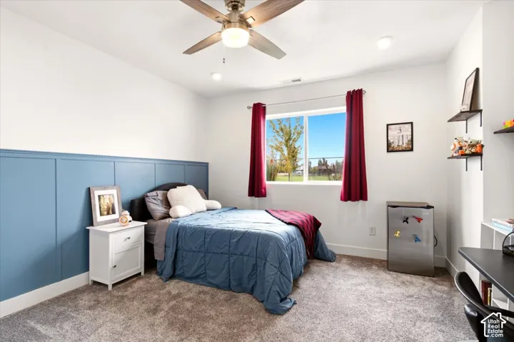 Bedroom featuring blue wainscoting, carpeted flooring, a ceiling fan with integrated light, and large windows