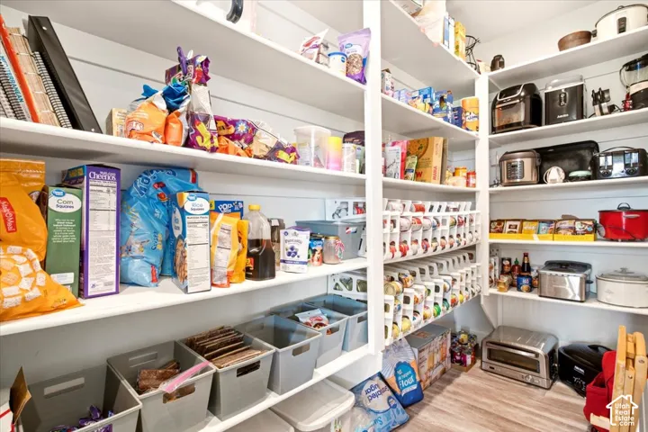 Walk-in pantry featuring white shiplap walls, extensive built-in shelving, and wood-finish flooring