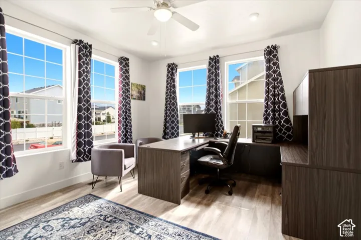 Room featuring light-toned wood-finish flooring, multiple windows with grid detailing, and a neutral color palette, finished with a white ceiling fan including integrated lighting