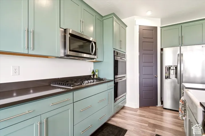 Kitchen featuring sage green cabinetry, stainless steel double wall ovens, gas cooktop, solid-surface countertops, and wood-finish flooring