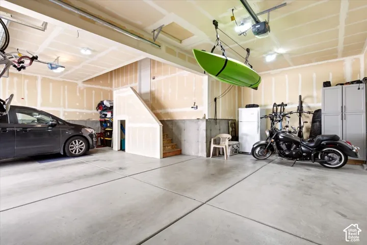 Multi-vehicle garage featuring concrete flooring, exposed wall studs, overhead lighting, and an enclosed staircase structure
