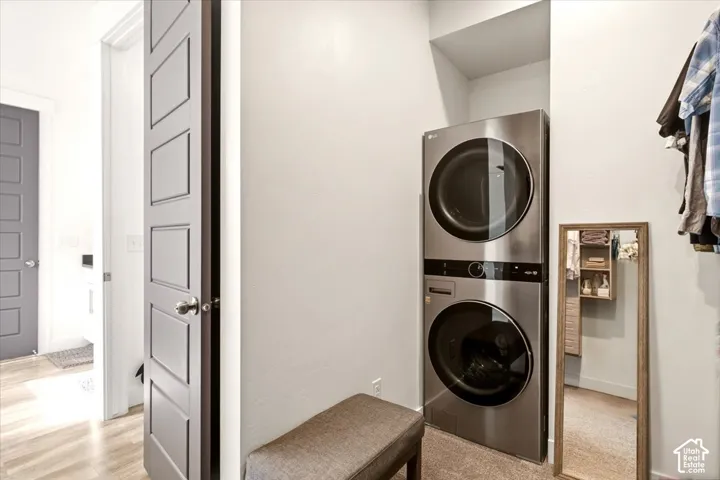 Stacked stainless steel laundry appliances situated within a dedicated niche, featuring a wood-finish interior door and neutral wall finishes