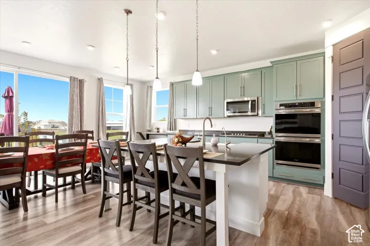 Kitchen featuring sage green cabinetry, dark stone countertops, an island with pendant lighting, stainless steel double wall ovens, and wood-finish flooring