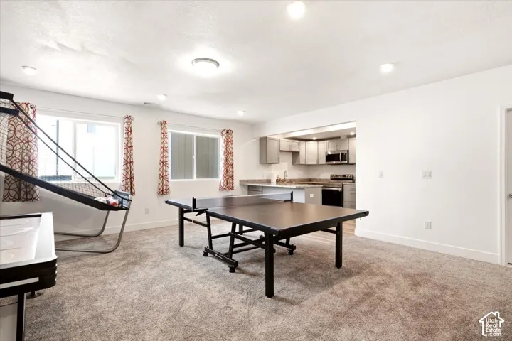 Open-concept area featuring neutral carpeting, recessed lighting, and kitchen equipped with cabinetry, countertops, and stainless-steel appliances