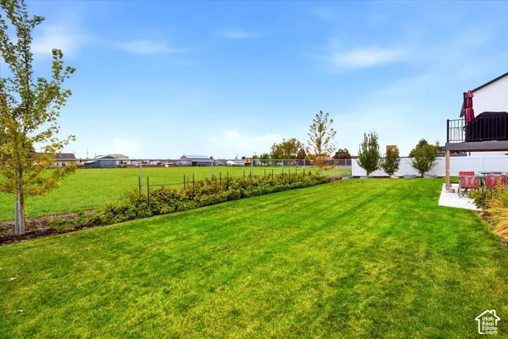 Expansive backyard featuring a manicured lawn, perimeter chain-link fencing, landscaping shrubbery, and a concrete patio