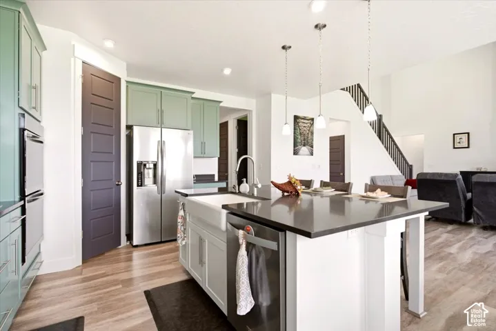 Kitchen featuring light-colored shaker cabinetry, dark solid-surface countertops, a farmhouse-style apron sink, stainless steel built-in appliances, and wood-finish flooring