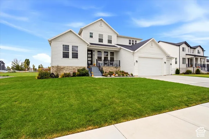 Multi-level residence featuring horizontal lap siding, stone veneer accents, a multi-gable roofline, and a paved concrete driveway leading to a multi-car garage
