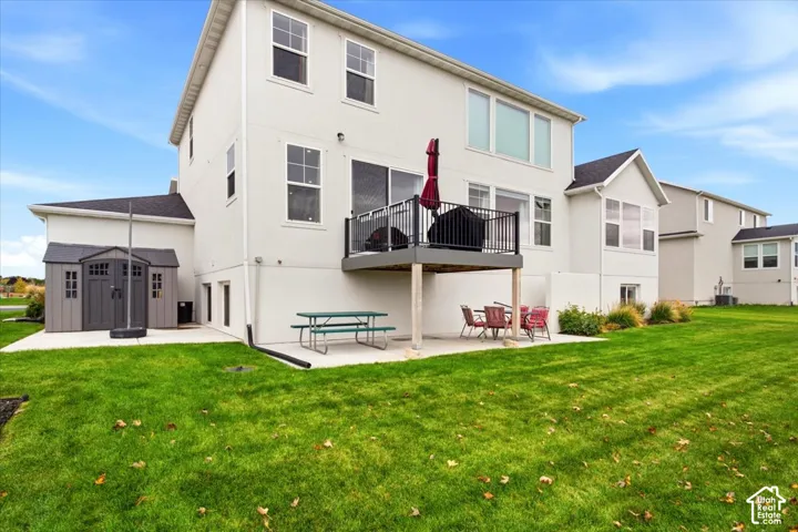 Exterior featuring a multi-level layout with a raised deck, metal railing, concrete patio, and a dedicated storage structure, all set within a expansive grass yard