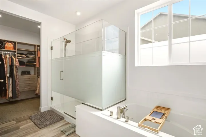 Glass-enclosed shower with frosted detailing, soaking tub with deck-mounted faucet, and built-in closet cabinetry featuring wood-finish shelving and drawers