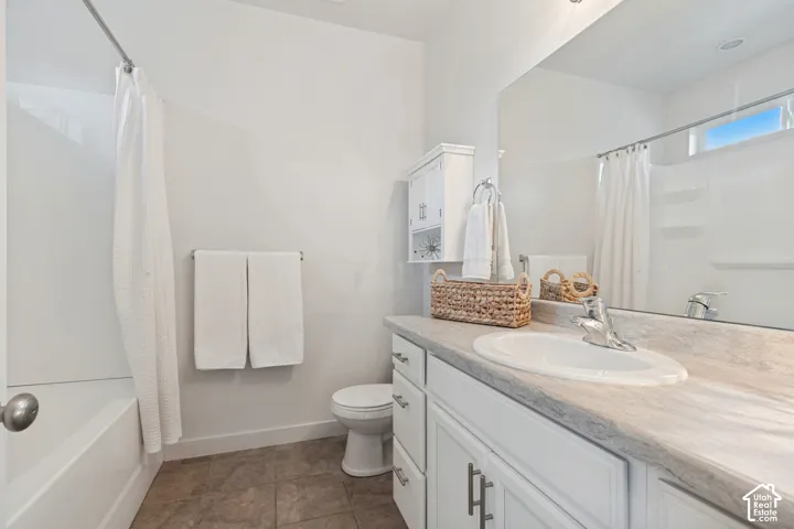 Bathroom featuring a vanity with a stone-finish countertop, oval undermount sink, white shaker-style cabinetry, tile flooring, and a shower-tub combination with a wall-mounted faucet