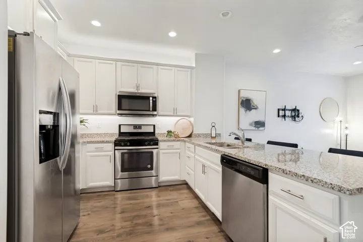 Kitchen featuring white cabinetry, stone-finish countertops, stainless steel appliances, recessed lighting, and wood-finish flooring