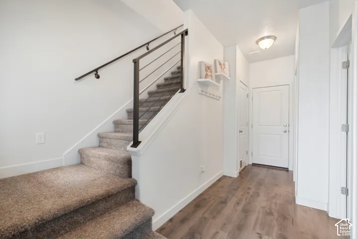 Entryway featuring wood-finish flooring, staircase with carpeted treads, and a metal horizontal-bar handrail