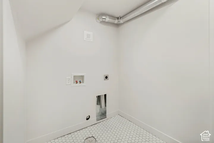 Utility alcove featuring hexagonal tile flooring, wall-mounted laundry supply valves, a recessed dryer vent, and exposed metal ductwork