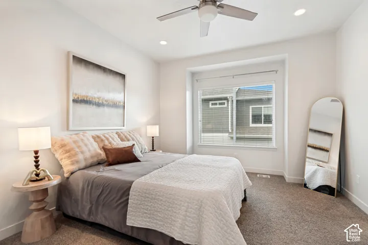Neutral-toned carpeted flooring, recessed ceiling lighting, brushed metal ceiling fan, and window with recessed alcove framing