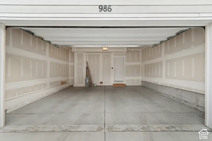 Two-car garage featuring a concrete floor, finished drywall, ceiling-mounted lighting, and a private exterior access door