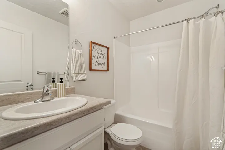 Bathroom featuring a white vanity with a neutral-toned countertop, integrated oval sink, chrome-finish faucet, and a combination tub and shower surround