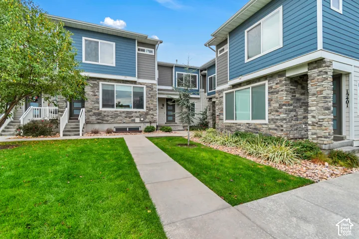 Multi-level exterior featuring horizontal lap siding, stacked stone masonry, concrete walkways, and manicured lawn landscaping