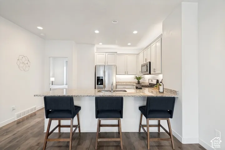 Kitchen featuring a stone-surface island, white shaker-style cabinetry, recessed ceiling lighting, and wood-finish flooring