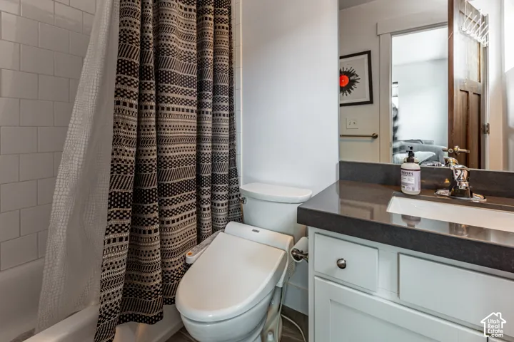 Bathroom featuring a white vanity cabinet, dark stone countertop, integrated sink with chrome faucet, and white subway tile shower surround