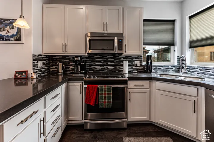Kitchen featuring white cabinetry, dark countertops, stainless steel appliances, a multi-tone linear mosaic backsplash, and wood-finish flooring