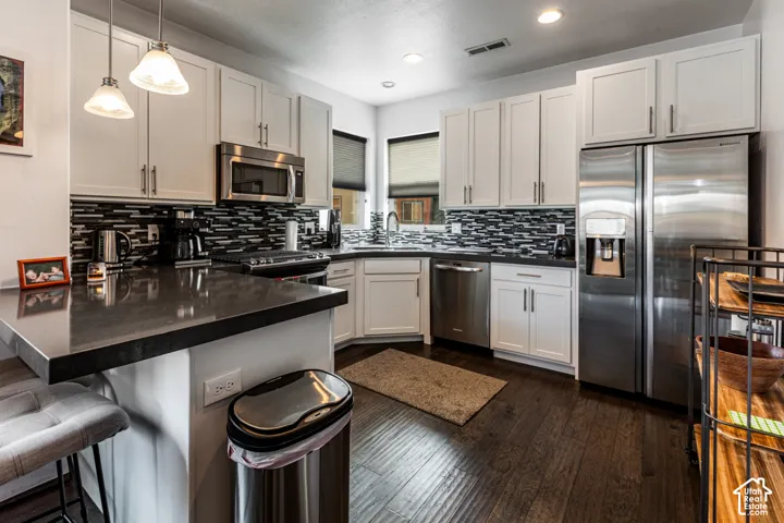 Kitchen featuring white cabinetry, dark stone countertops, stainless steel appliances, a multi-tonal linear tile backsplash, and wood-finish flooring