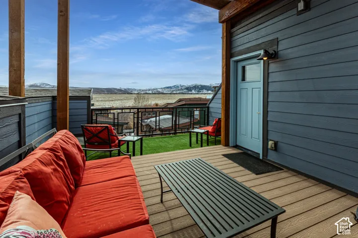 Covered outdoor deck featuring horizontal wood-plank style composite decking, synthetic lawn inset, metal-frame railing, and mountain backdrop