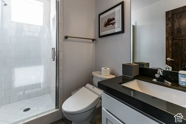 Bathroom featuring a glass-enclosed shower with white tiled walls, a dark stone vanity countertop, a rectangular under-mount sink, and a dark wood-finish door