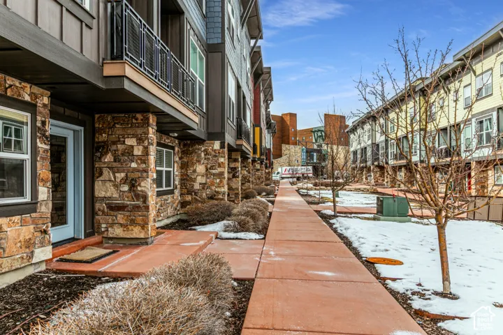 Multi-story building exterior featuring stone masonry cladding, vertical siding, metal balconies, and a paved concrete walkway