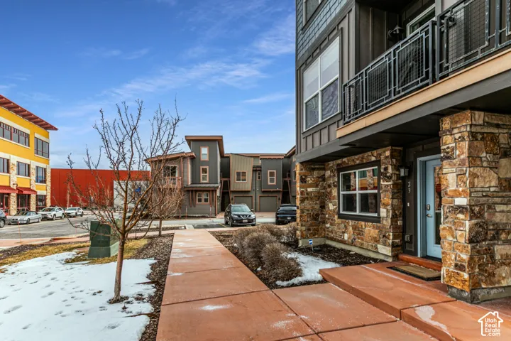 Multi-story residential exterior featuring natural stone veneer, mixed-material siding, metal-railed balconies, and concrete walkways