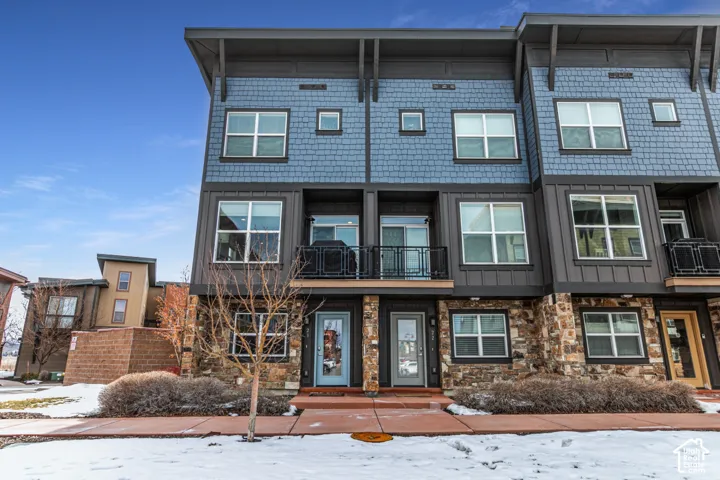 Multi-level contemporary exterior featuring shingle-style siding, stone veneer masonry, metal-framed balconies, and expansive multi-pane windows