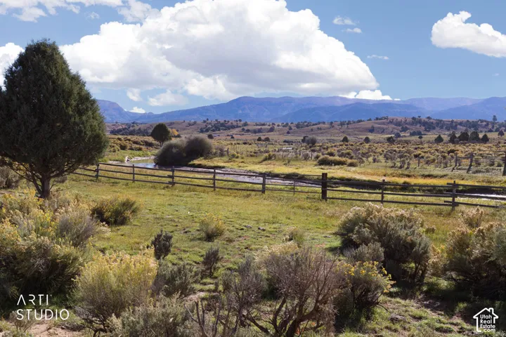 Expansive acreage featuring a natural creek, split-rail perimeter fencing, mature trees, and a mountain backdrop