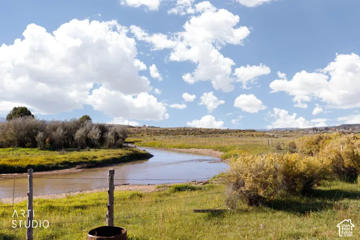 Natural creek frontage featuring mature riparian vegetation, open meadow landscape, and post-and-wire fencing