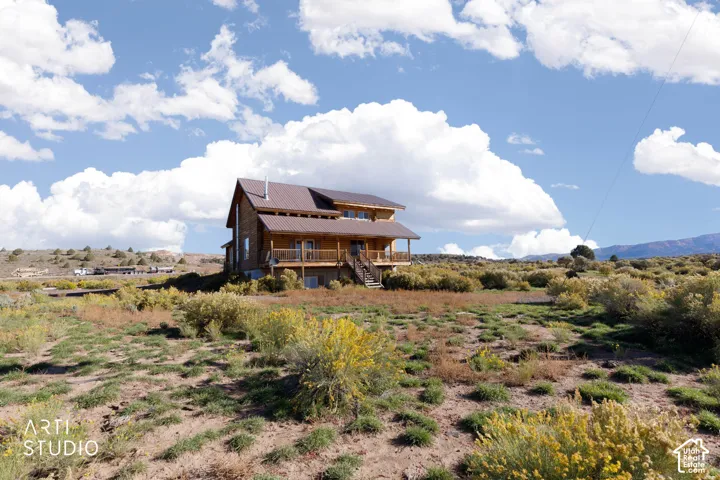 Rustic timber-frame residence featuring a metal roof, tiered covered porch with wood railing, stone foundation, and expansive natural landscape