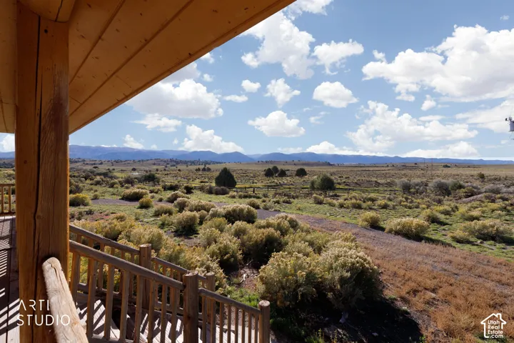 Covered timber-frame porch featuring natural log support columns and railings, overlooking an expansive landscape with prominent mountain ranges