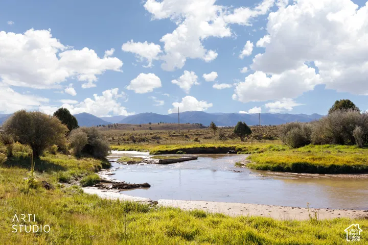 Expansive landscape featuring a winding natural waterway, mature trees, open grasslands, and a mountainous backdrop