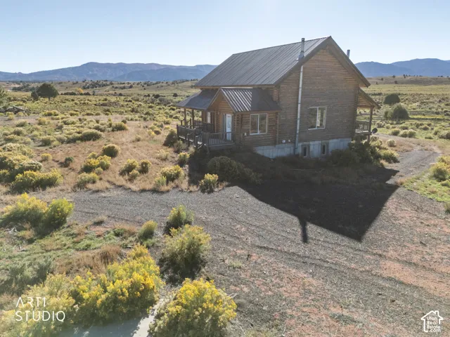 Log cabin exterior featuring horizontal log siding, a metal roof, and an expansive wraparound deck, set against a mountainous horizon