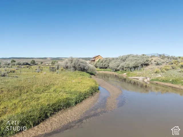 Natural creek frontage with expansive grassy meadow, native brush, and post-and-rail fencing