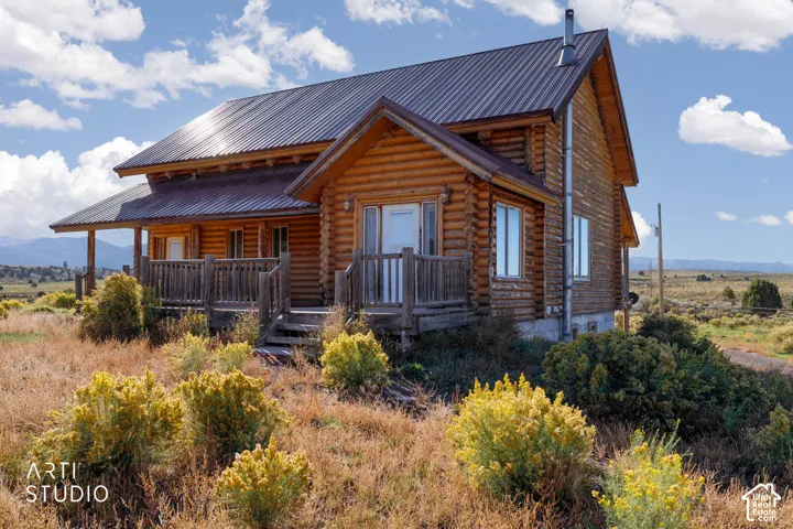 Log exterior cabin featuring a metal roof, wraparound wooden deck, and a vertical metal chimney