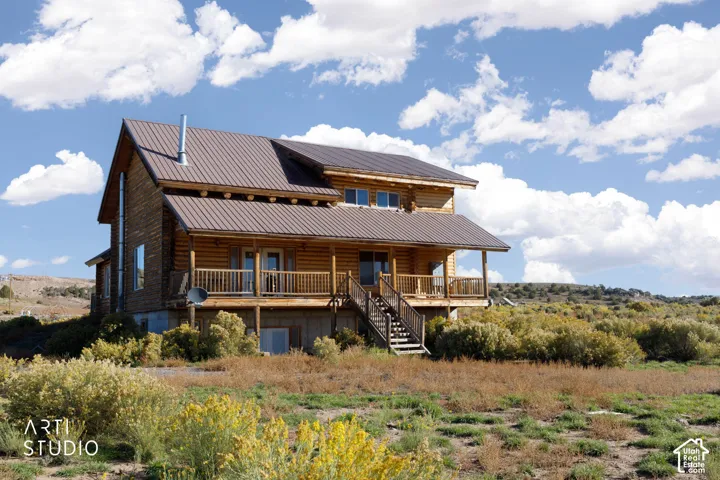 Log cabin exterior featuring horizontal log construction, a standing-seam metal roof, a full-length covered porch with wooden railings, and a concrete foundation